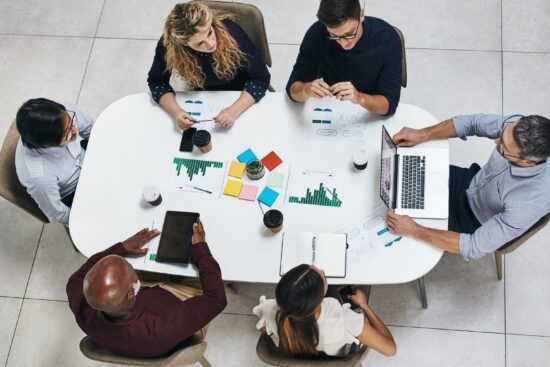 A diverse group of individuals collaborates around a table, each using their laptops for a productive meeting.