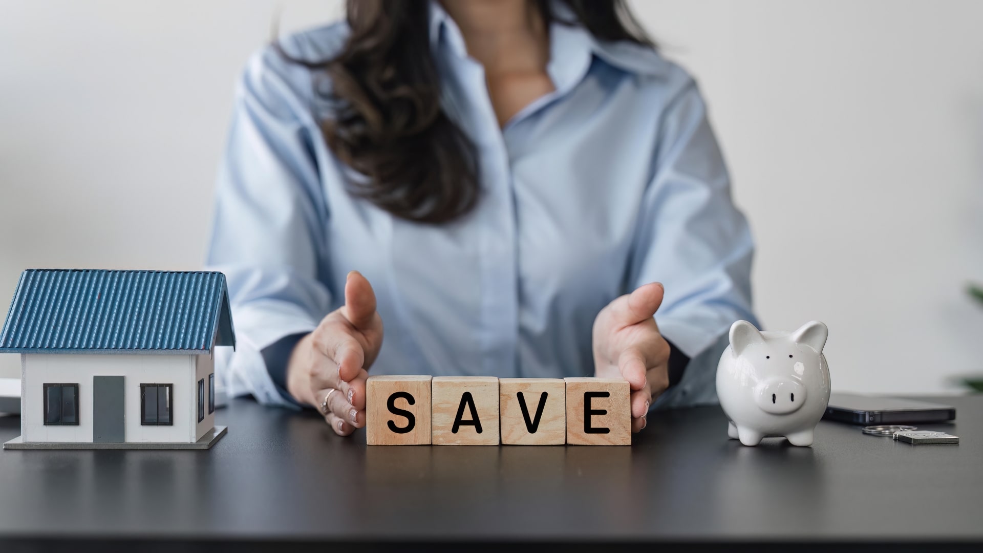 A woman is holding a block that displays the word "save," positioned on a table in a well-lit environment.