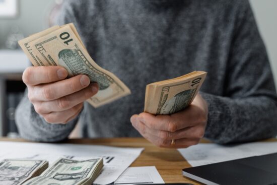 A man holds cash in front of a laptop, symbolizing financial success and online transactions.