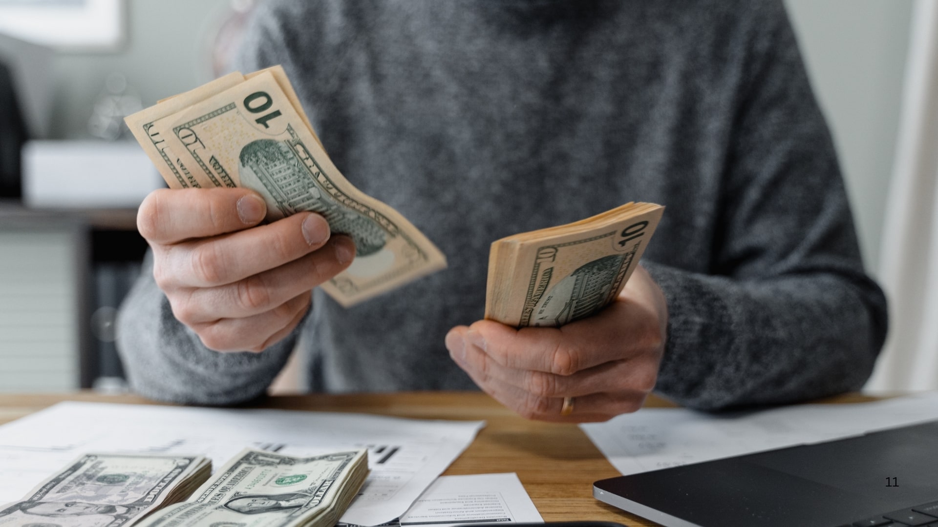 A man holds cash in front of a laptop, symbolizing financial success and online transactions.