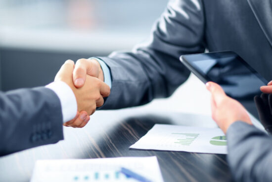 Two business professionals shaking hands over a conference table, symbolizing agreement and collaboration in a professional setting Banks.