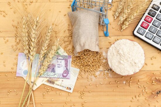 A wooden table displays wheat, a stack of money, and a calculator, symbolizing agriculture and finance.